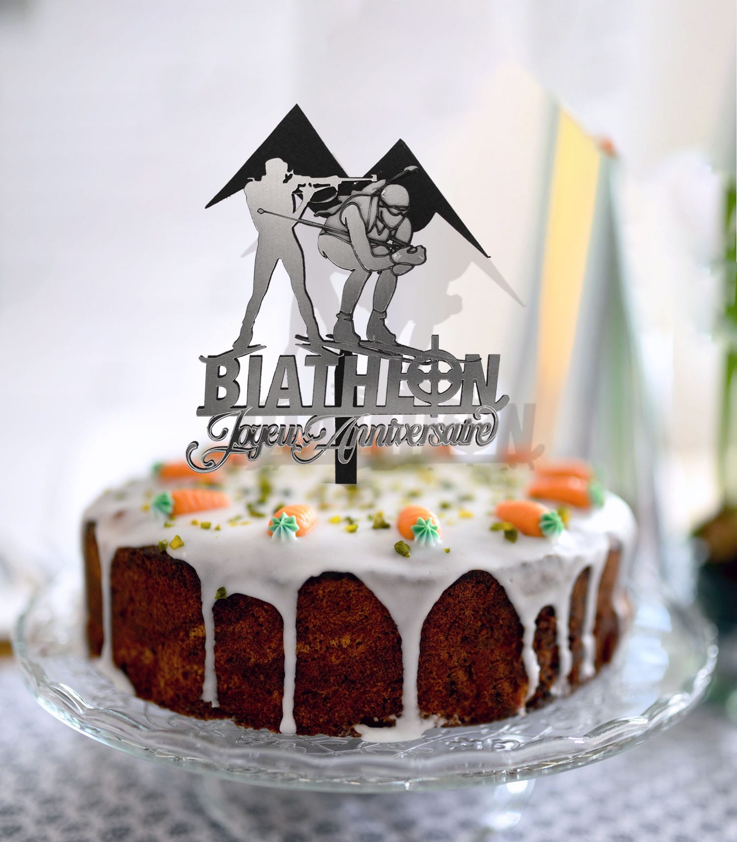 Topper à gâteau biathlon en bois peint blanc, silhouettes de deux athlètes (carabine et ski) avec deux monts en arrière-plan, inscription Joyeux anniversaire en argent miroir